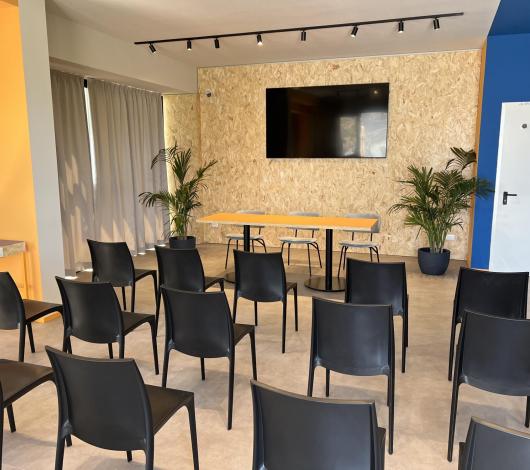 Sala conferenze moderna e luminosa con sedie nere e piante verdi.