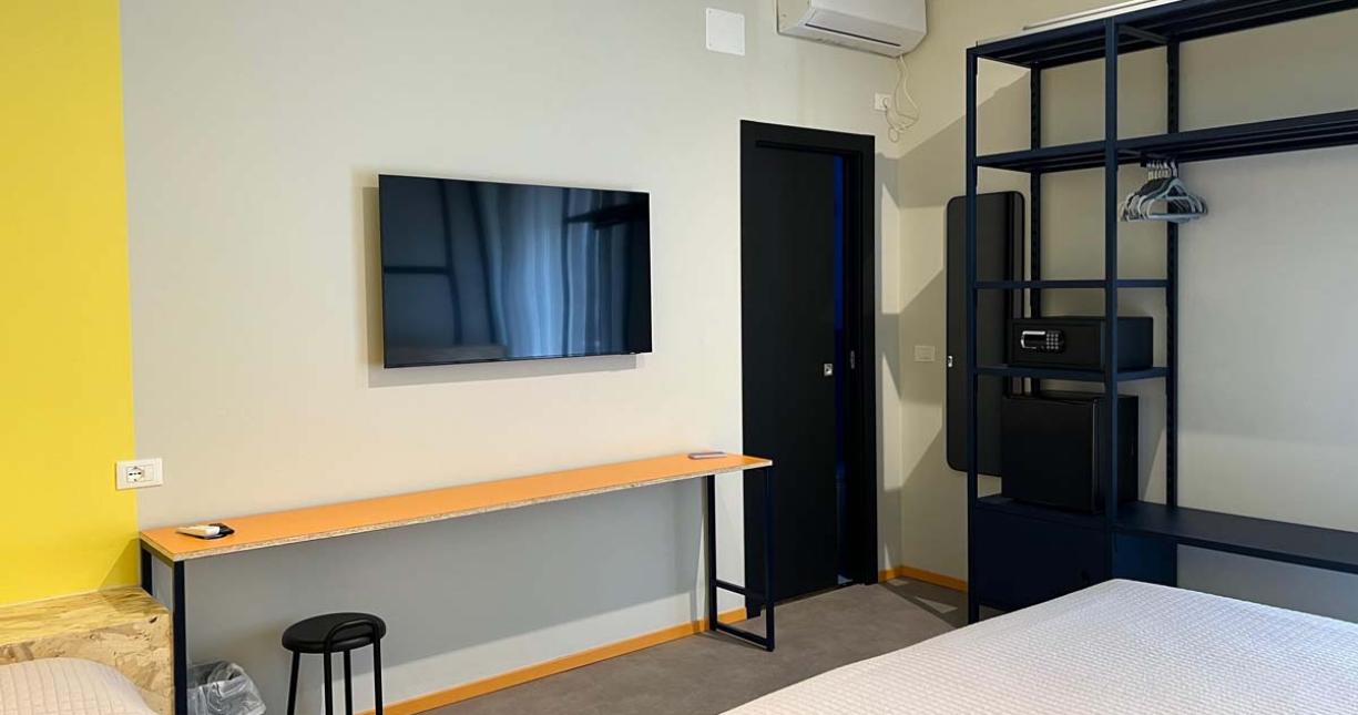 Camera moderna e accogliente con TV, scrivania e armadio aperto.